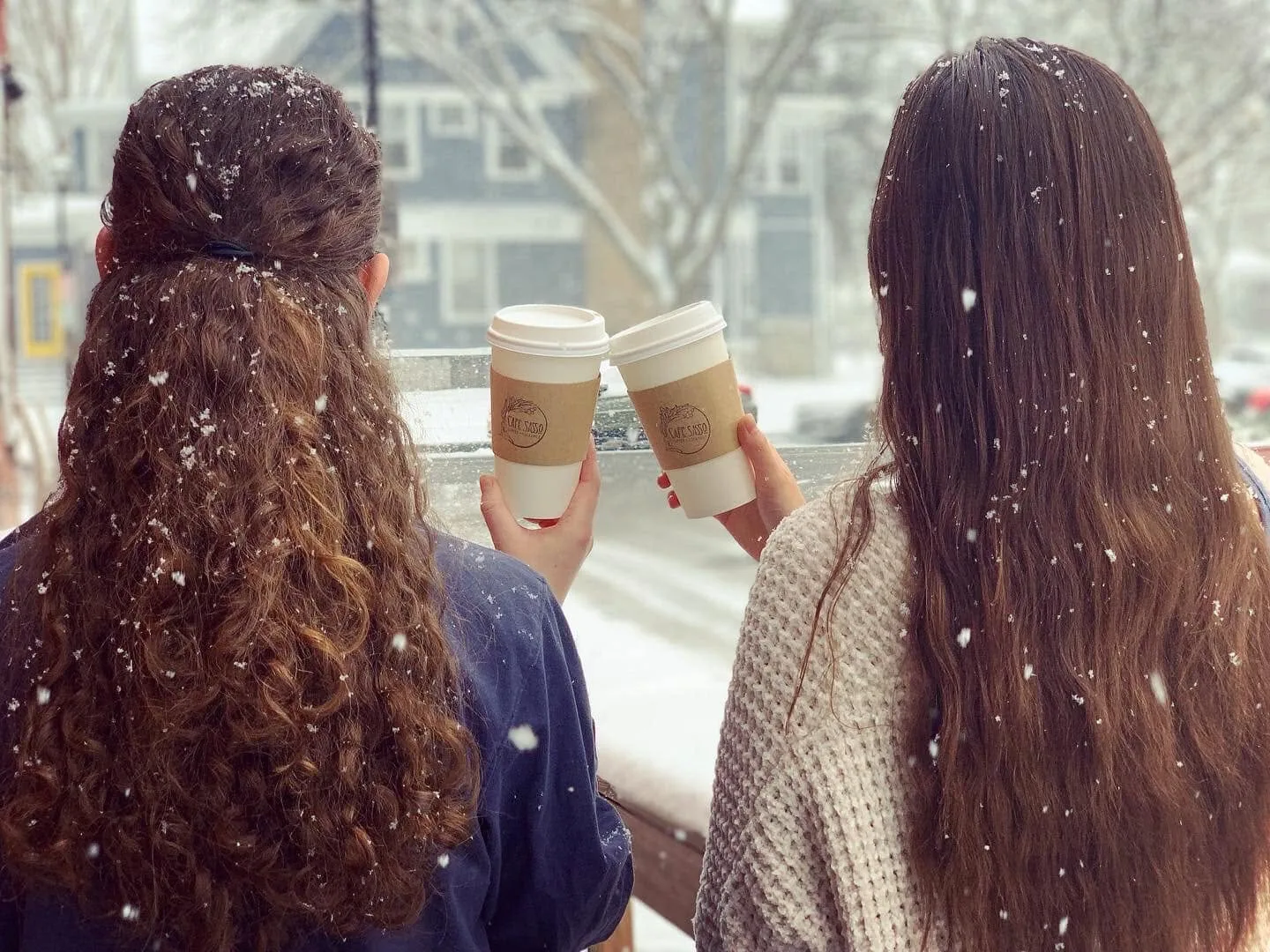 Two customers at the window, cups in hand, watching snow fall on Park Avenue