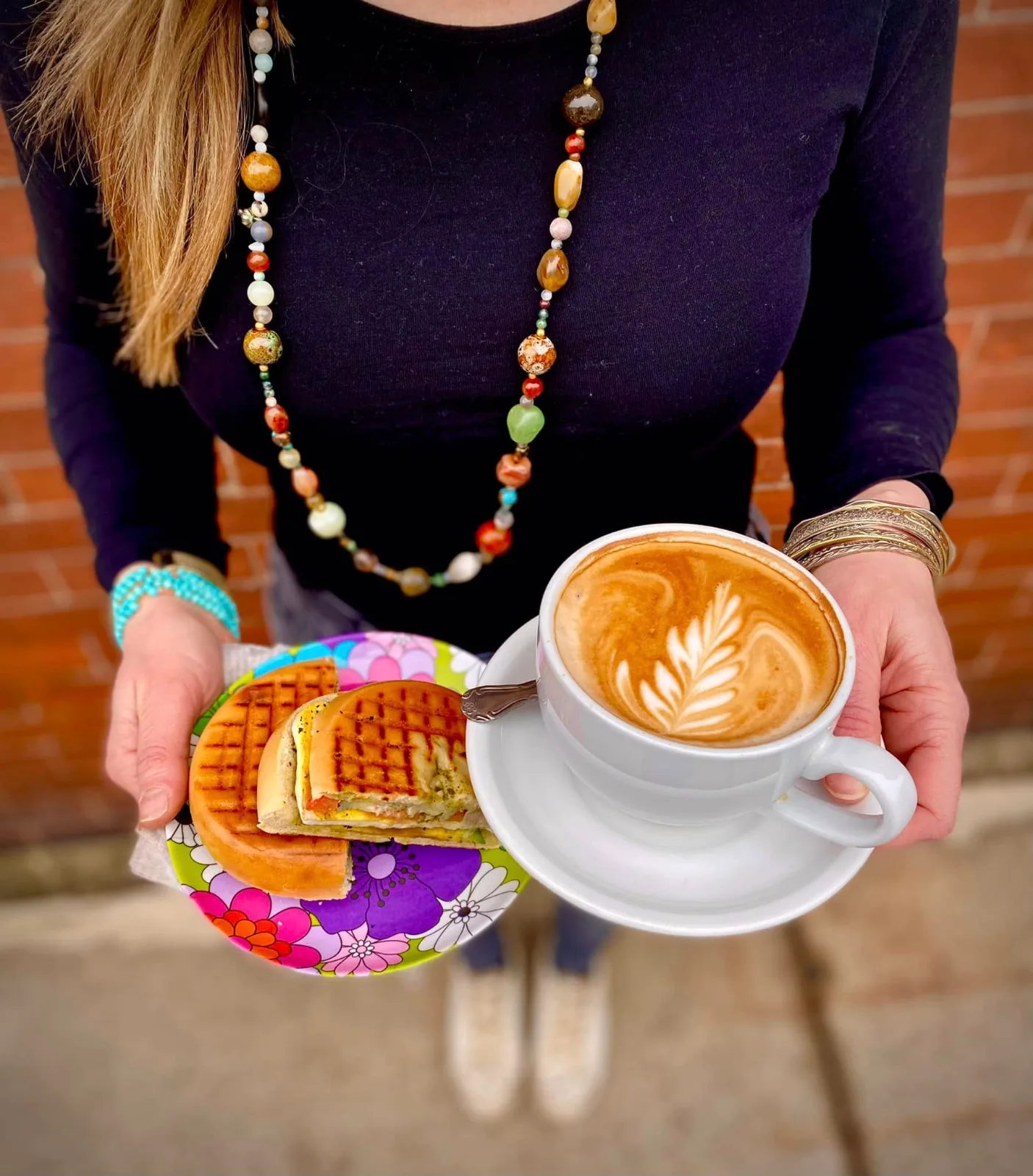 A server carrying a cappuccino and a plate of waffle sandwiches outside the cafe