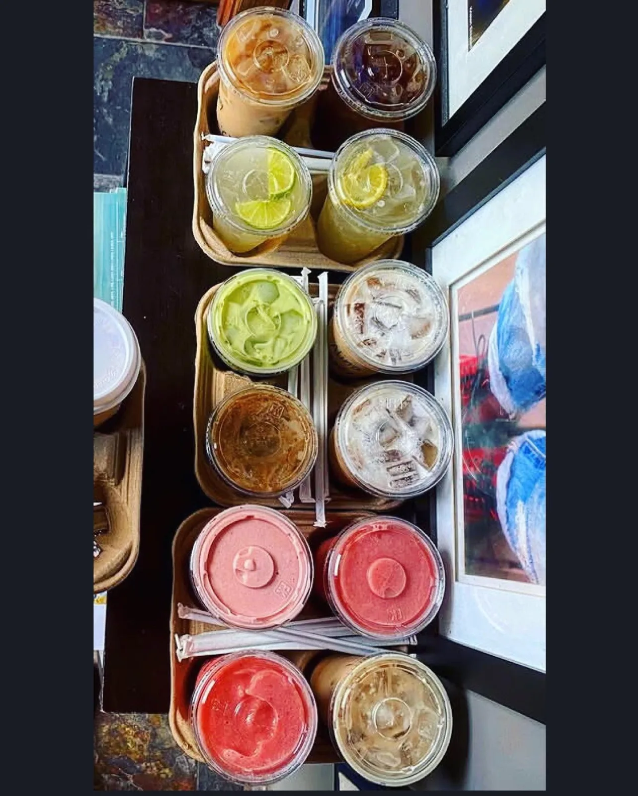 A tray of iced drinks in takeaway cups, including matcha and iced coffee, with sliced limes