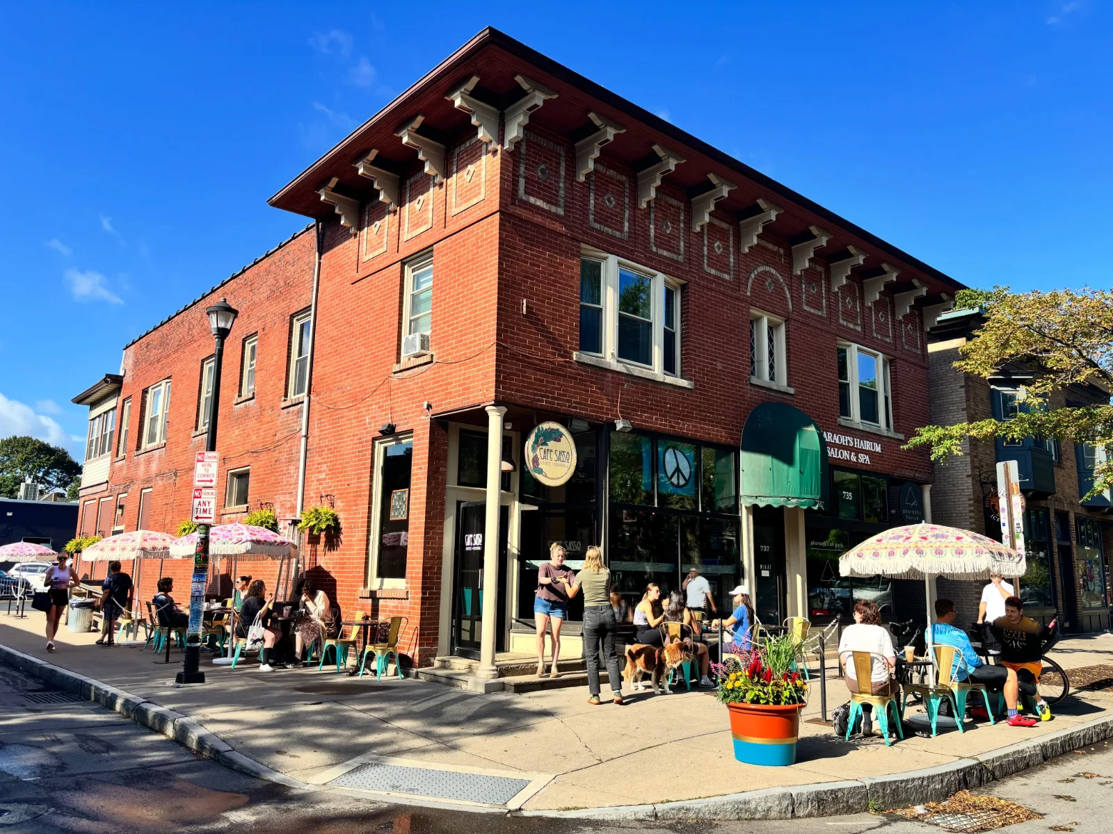 The cafe on a red brick corner building, with people at teal tables under umbrellas on the sidewalk