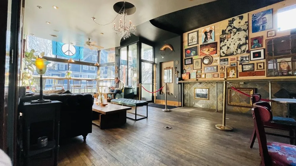 The lounge inside the cafe: a leather sofa and low table under a chandelier, beside a wall hung with framed pictures